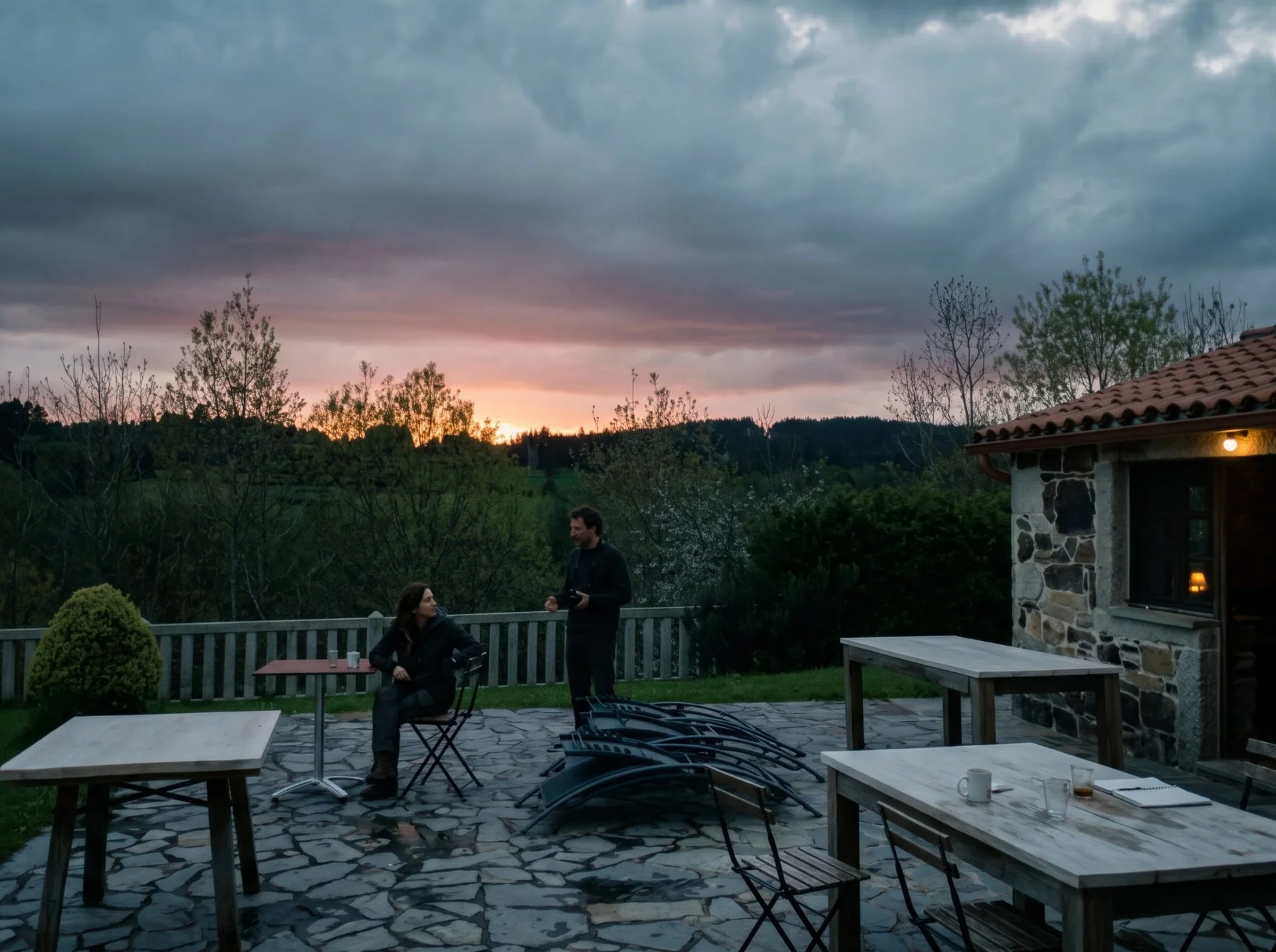 Dos personas conversan en la terraza de As Casiñas mientras cae el sol sobre Porto de Bois